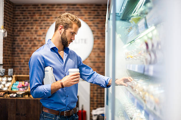 young man choosing food from cooling shelf in a coffee shop - junk food stock pictures, royalty-free photos & images