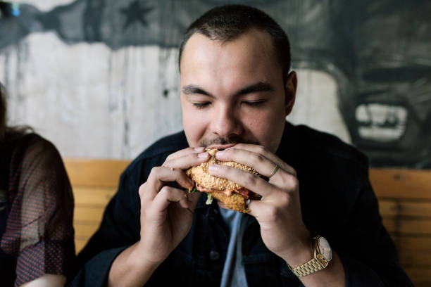 young man eating a burger - junk food stock pictures, royalty-free photos & images