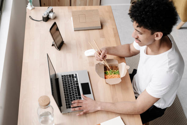 young man eating chinese food while working from home - junk food stock pictures, royalty-free photos & images
