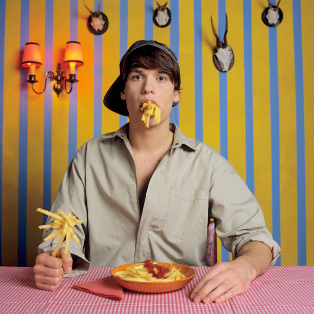 young man eating french fries - junk food stock pictures, royalty-free photos & images