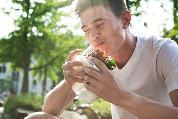 young man eating hamburger - junk food stock pictures, royalty-free photos & images