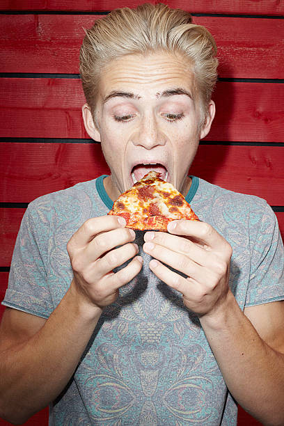 young man eating pizza - junk food stock pictures, royalty-free photos & images