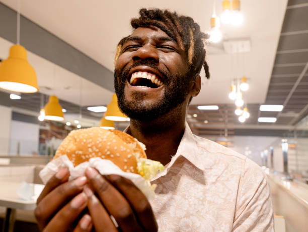 young man enjoying having burger at a restaurant - junk food stock pictures, royalty-free photos & images