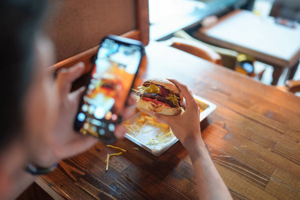 young man is taking a photo of his burger with his phone - food stock pictures, royalty-free photos & images