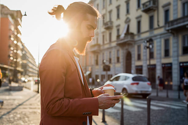 young man with coffee to go looking at cell phone - junk food stock pictures, royalty-free photos & images