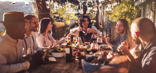 young multi-ethnic friends dining at rustic countryside restaurant at sunset - food stock pictures, royalty-free photos & images