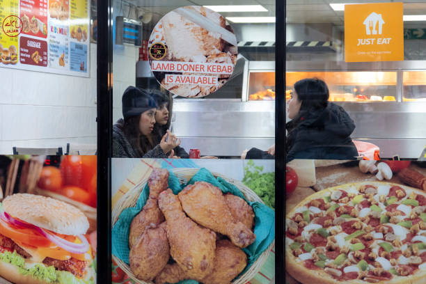 Young people sitting down inside to eat in a fast food restaurant where images of the foods available adorn the exterior on 14th December 2023 in...