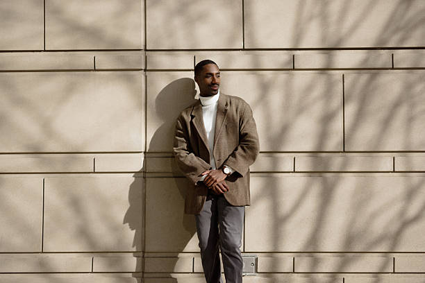 young professional standing confidently against a sunlit wall outdoors - fashion stock pictures, royalty-free photos & images