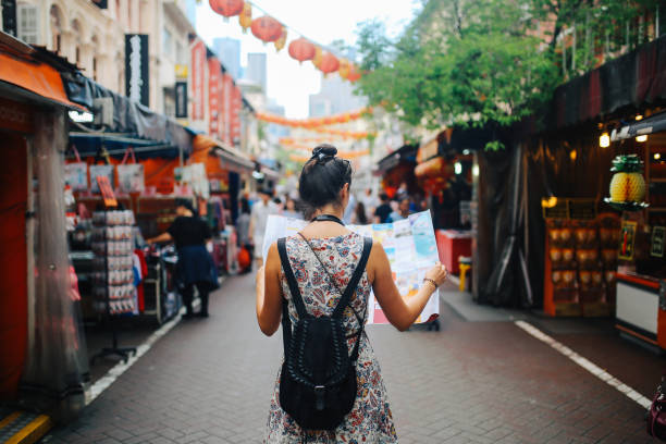 young solo traveler woman in singapore street market checking the map - travel stock pictures, royalty-free photos & images