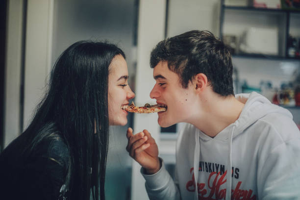 young teenager copule sharing slice of pizza at home - food stock pictures, royalty-free photos & images