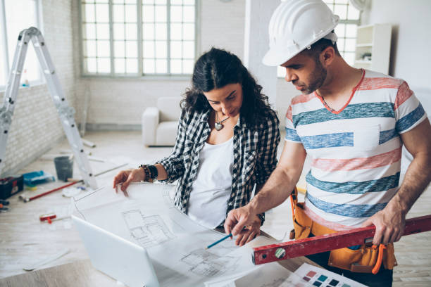 young woman and construction worker looking at blueprints - home decoration stock pictures, royalty-free photos & images