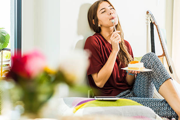 young woman at home enloying piece of cake in bed - food stock pictures, royalty-free photos & images