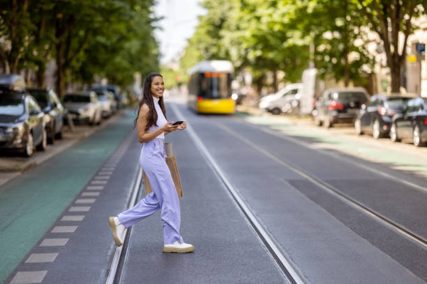 young woman crossing the street with mobile phone. - fashion photos et images de collection