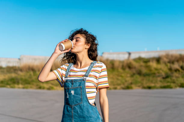 young woman drinking coffee from a disposable cup - junk food stock pictures, royalty-free photos & images