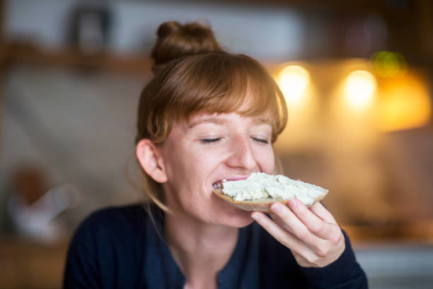 young woman eating bread with cream cheese - food stock pictures, royalty-free photos & images