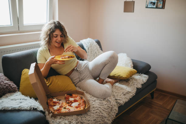 young woman eating pizza in living room - junk food stock pictures, royalty-free photos & images