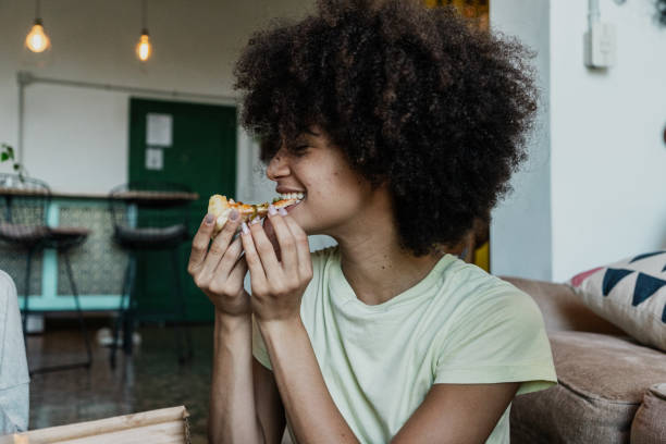 young woman eating slice pizza in the living room at home - junk food stock pictures, royalty-free photos & images