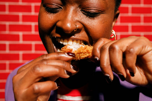 young woman enjoying chicken wings in front of red brick wall - junk food stock pictures, royalty-free photos & images