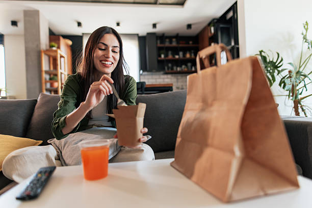 young woman enjoying takeaway food at home - junk food stock pictures, royalty-free photos & images
