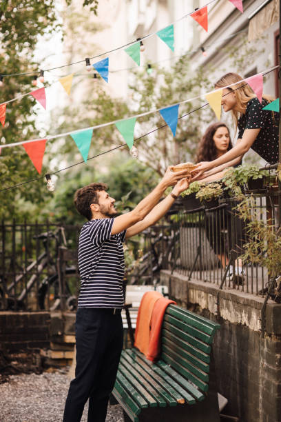 young woman giving food to smiling male friend from balcony during garden party - garden decoration stock pictures, royalty-free photos & images