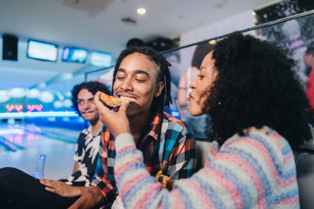 young woman giving pizza to her friend at a bowling club - food stockfoto's en -beelden
