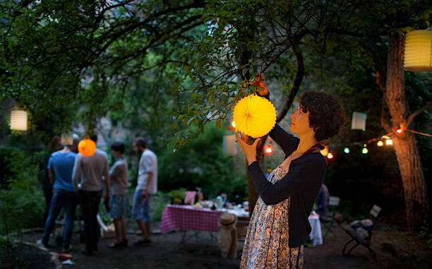 young woman hanging paper lantern on tree in back yard - garden decoration stock pictures, royalty-free photos & images