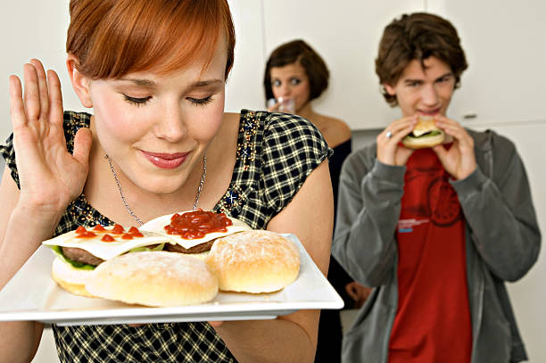 young woman holding burgers in a tray with her friends in background - junk food stockfoto's en -beelden