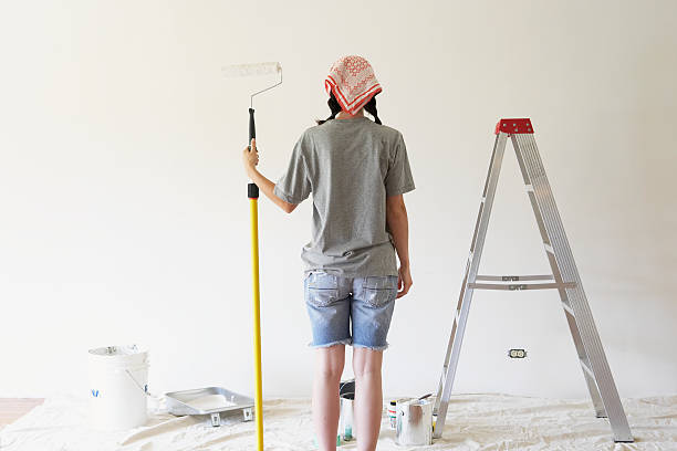 young woman holding paint roller, rear view - home decoration stock pictures, royalty-free photos & images