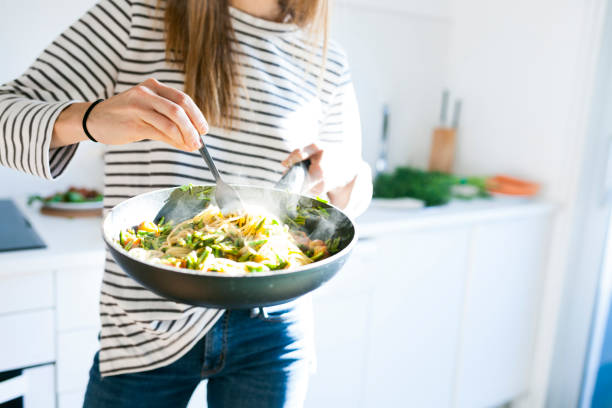 young woman holding pan with vegan pasta dish - food stock pictures, royalty-free photos & images