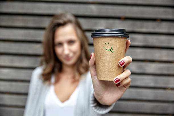 young woman holding takeaway coffee cup with smiley face - junk food stock pictures, royalty-free photos & images