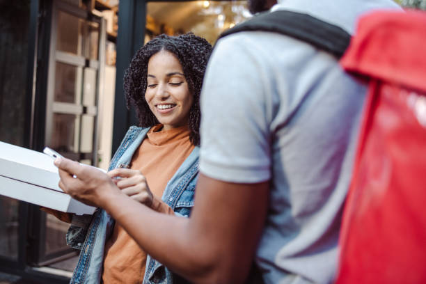 young woman holds the ordered food and signs the receipt on the smart phone - junk food stock pictures, royalty-free photos & images