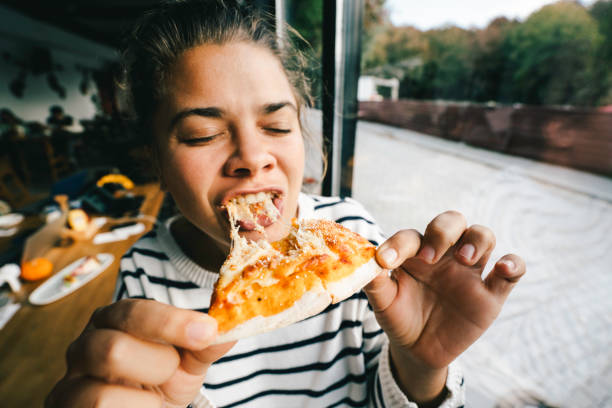 young woman is eating cheese pizza with pleasure - junk food stock pictures, royalty-free photos & images
