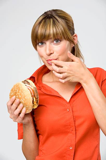 young woman licking finger, holding hamburger, portrait, close-up - junk food stock pictures, royalty-free photos & images