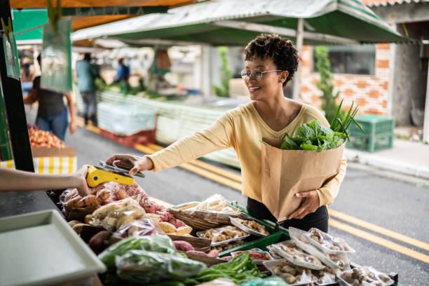 young woman paying with mobile phone at a street market - food stock pictures, royalty-free photos & images