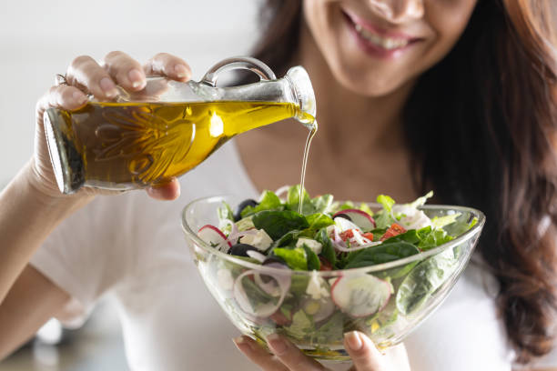 young woman pouring olive oil in to the salad. healthy lifestyle eating concept. - food stock pictures, royalty-free photos & images