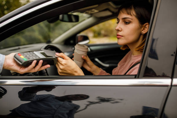 young woman sitting in her car and paying for takeaway coffee with credit card to a service person - junk food stock pictures, royalty-free photos & images