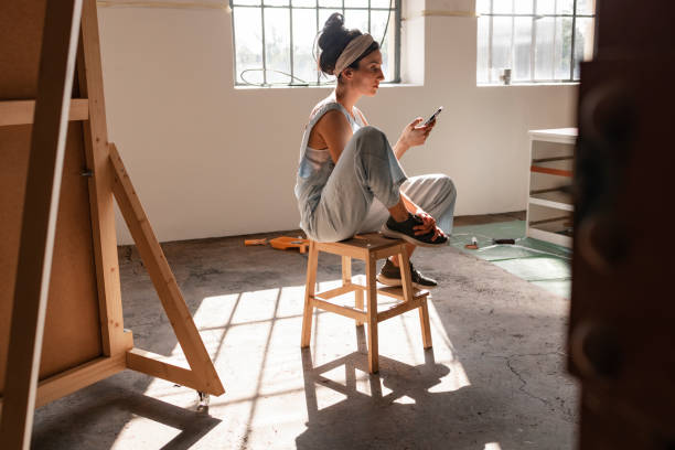 young woman sitting on a chair and using mobile phone - home decoration stock pictures, royalty-free photos & images