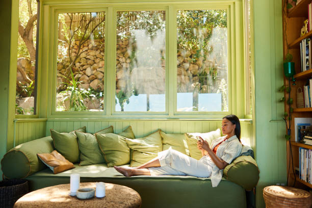 young woman sitting on her sofa and texting on her phone - home decoration stock pictures, royalty-free photos & images