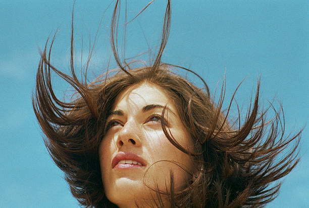 young woman standing outdoors, hair blowing, close-up - hairstyle stock pictures, royalty-free photos & images