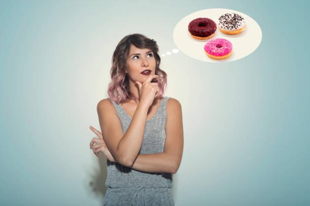 young woman thinking about an assortment of donuts - junk food stock pictures, royalty-free photos & images
