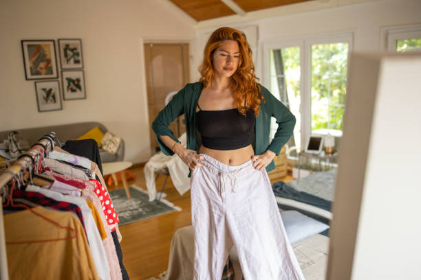 young woman trying on a shirt she picked out in her bedroom at home - fashion stock pictures, royalty-free photos & images