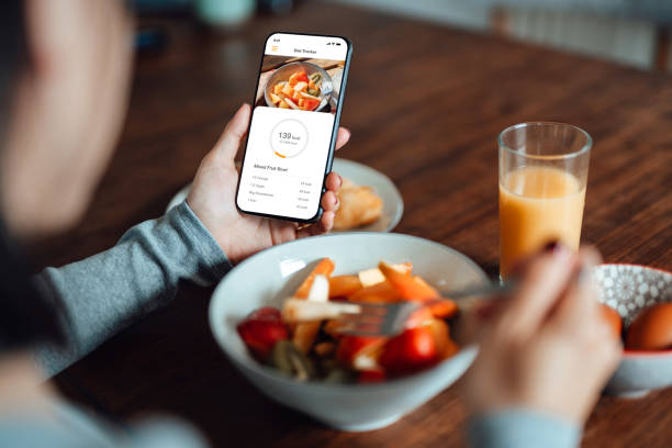 young woman using mobile app to track nutrition and count calories with smartphone - food stock pictures, royalty-free photos & images