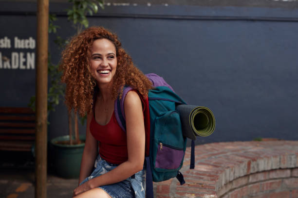 young woman with backpack smiling, while sitting in courtyard - travel stockfoto's en -beelden