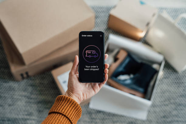 your order has been shipped - close up shot of hand holding smartphone with online shopping box stack at the background - fashion stock pictures, royalty-free photos & images