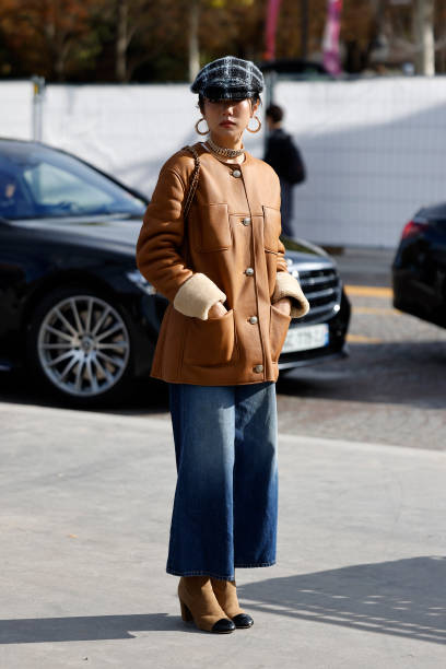 Yoyo Cao wears brown jacket, brown Chanel bag with fur detail, black checked hat, blue jeans, brown boots, outside Chanel, during Womenswear...