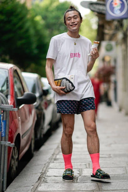 Yu Masui wears a white t-shirt with the word "Goth" prined in pink, a clutch, a short, pink socks, sandals, and s holding an ice cream, outside the...