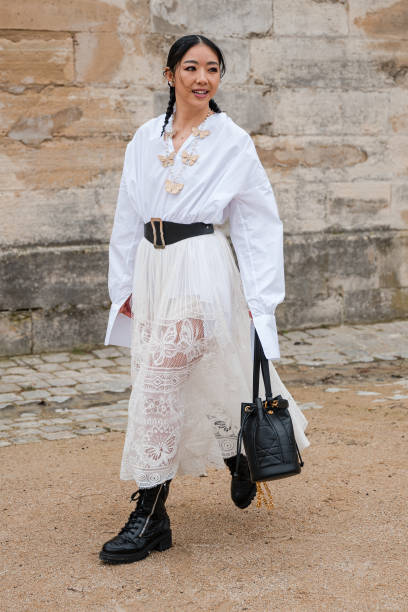 Yuwei Zhangzou wears white shirt, cream lace maxi skirt, black belt, black Dior bag, black boots, outside Dior, during the Womenswear Fall/Winter...