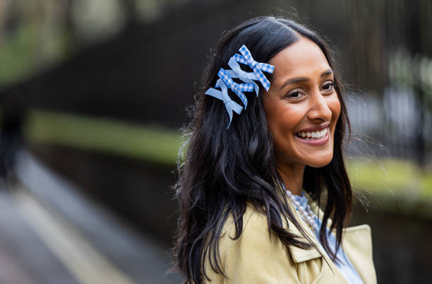 Zeena Shah wears blue bows in hair, blue dress, pearl necklace, beige coat, blue bag outside Eudon Choi during London Fashion Week February 2024 on...
