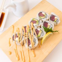 a bamboo cutting board sits with a sushi maki roll made with tuna, avocado and cream cheese - junk food stock pictures, royalty-free photos & images