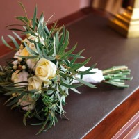 a beautiful wedding bouquet lies on the table, chest of drawers or bedside table, close-up. bouquet of different flowers and green leaves, tied with a satin ribbon, blurred background. wedding theme. a beautiful combination o